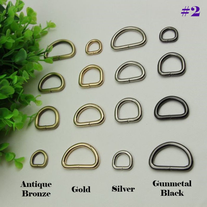 May include: Assortment of D-rings in four finishes: antique bronze, gold, silver, and gunmetal black. The D-rings are arranged in rows by finish and size, with the smallest D-rings at the top and the largest at the bottom.
