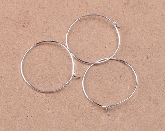 May include: Three silver hoop earrings, each with a simple circular design. The earrings are arranged in a loose pile on a brown surface.