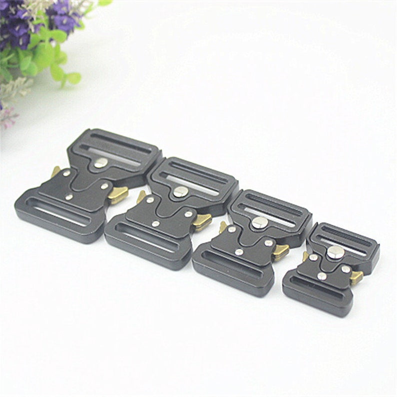 May include: Four black metal belt buckles of different sizes with gold-colored clasps. The buckles are arranged in a row from largest to smallest.
