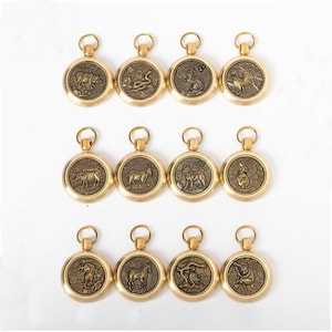 May include: Twelve gold-coloured pendants, each displaying a different zodiac animal in relief. The round pendants have a small loop at the top for hanging. Animals include a bull, snake, lion, and rabbit. The pendants are likely made of brass.