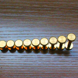 May include: A row of ten gold-coloured metal knobs, arranged in a line on a wooden surface.