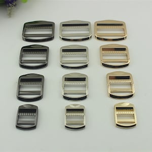 May include: Assortment of metal slider buckles in black, silver, and gold finishes. The buckles are rectangular with a rounded top and bottom. They have a center bar that slides through the strap.
