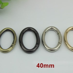 May include: Four oval-shaped metal key rings in different finishes: antique brass, black, silver, and gold. Each ring measures 40mm in diameter.