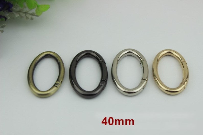 May include: Four oval-shaped metal key rings in different finishes: antique brass, black, silver, and gold. Each ring measures 40mm in diameter.