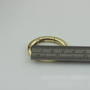 May include: Gold-toned metal ring with a spring-loaded clasp. The ring is measured with a ruler, showing it is approximately 3 inches in diameter.