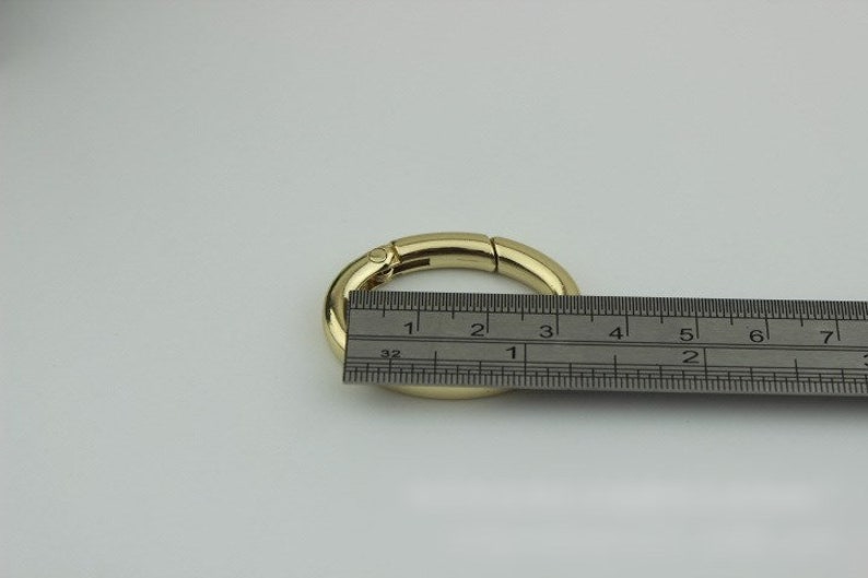 May include: Gold-toned metal ring with a spring-loaded clasp. The ring is measured with a ruler, showing it is approximately 3 inches in diameter.
