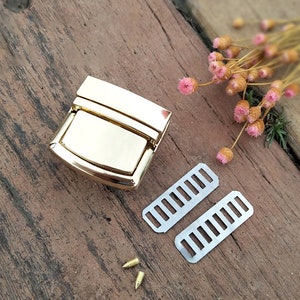 May include: Gold-toned metal clasp with a rectangular shape and a smooth, shiny finish. Two silver metal straps with rectangular holes are included, along with two small gold-toned metal pins.