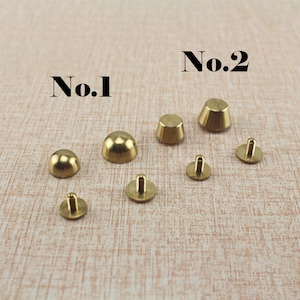 May include: Assortment of brass metal rivets, some with a domed top and others with a conical top. The rivets are labeled "No. 1" and "No. 2".