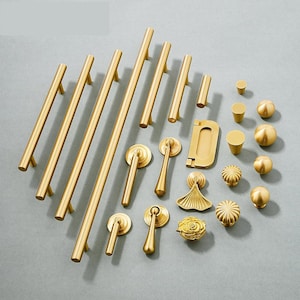 Może przedstawiać: Zbiór złotych okuć meblowych, w tym uchwytów, gałek i pokręteł do szuflad. Okucia są ułożone na jasnoszarym tle.