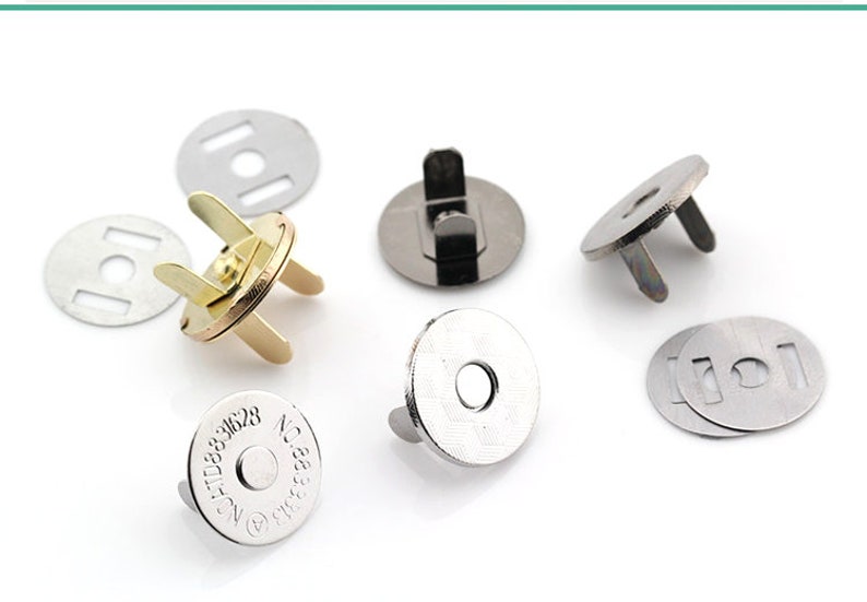 May include: Assortment of silver and gold magnetic snaps for sewing and crafting projects. The snaps have a round base with two prongs on the top. Some snaps have a metal ring in the center of the base. One snap has the text "No. 31628" printed on the base.