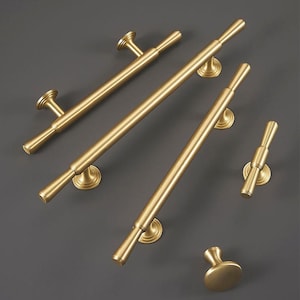 May include: Five gold-toned cabinet hardware pulls in various styles and sizes. The pulls are made of metal and have a polished finish.