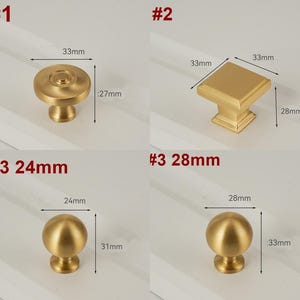 May include: Three gold cabinet knobs with measurements in inches. The first knob is round with a raised center. The second knob is square with a raised edge. The third knob is round with a smooth surface.