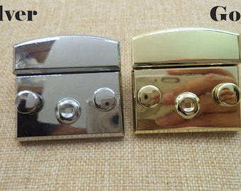 May include: Two metal clasps, one silver and one gold, with three round studs on each. The clasps are closed and have a rectangular shape.