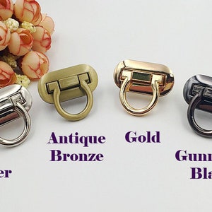 May include: Four metal clasps in different finishes: silver, antique bronze, gold, and gunmetal black. Each clasp has a rectangular base with a rounded, D-shaped ring.