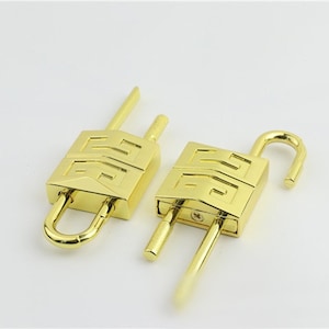 May include: Two gold-colored padlocks, one open and one closed, are displayed against a white background. The padlocks have a rectangular body with a stylized design and a curved shackle. The open padlock's shackle is raised.
