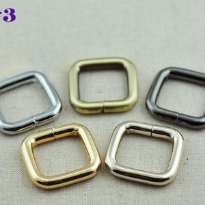 May include: Four square metal rings in different finishes: silver, gold, brass, and black. The rings are all the same size and have a smooth finish.