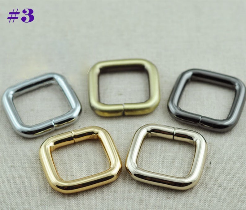 May include: Four square metal rings in different finishes: silver, gold, brass, and black. The rings are all the same size and have a smooth finish.