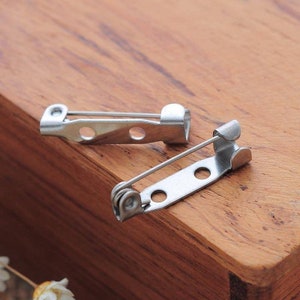 May include: Two silver-toned metal brooch backs with spring clasps and three holes for attaching a pin or other embellishment.