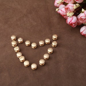 May include: A heart shape made of gold metal rivets on a brown surface. The rivets are arranged in a heart shape with the points of the heart facing up.