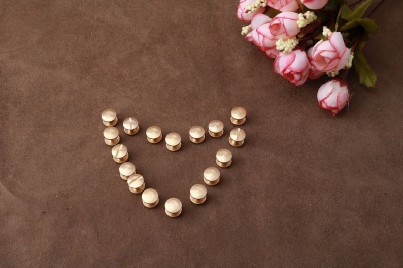 May include: A heart shape made of gold metal rivets on a brown surface. The rivets are arranged in a heart shape with the points of the heart facing up.