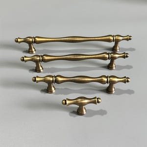 Peut inclure: Quatre poignées de tiroir en laiton antique de différentes tailles. Les poignées ont un design simple et élégant avec une forme légèrement incurvée.