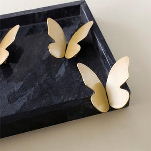 May include: Three gold butterfly-shaped drawer pulls on a black marble surface.