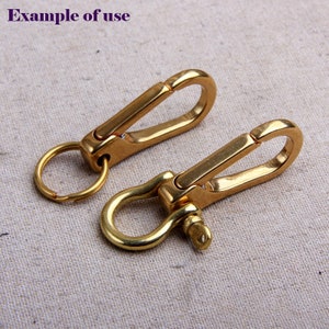 May include: Two brass-colored keychains with a carabiner-style clip and a ring. One keychain has a simple ring, while the other has a U-shaped shackle. The text "example of use" is in the upper left corner.