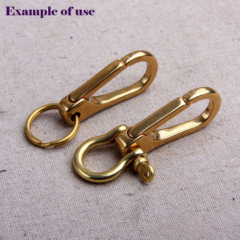 May include: Two brass-colored keychains with a carabiner-style clip and a ring. One keychain has a simple ring, while the other has a U-shaped shackle. The text "example of use" is in the upper left corner.
