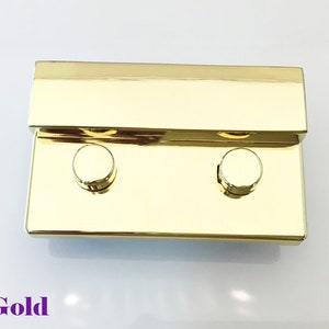 May include: Gold-toned metal clasp with two round knobs. The clasp is rectangular and has a shiny finish.