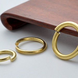 May include: Three gold-colored metal jump rings of different sizes. The rings are open and have a smooth, polished finish.
