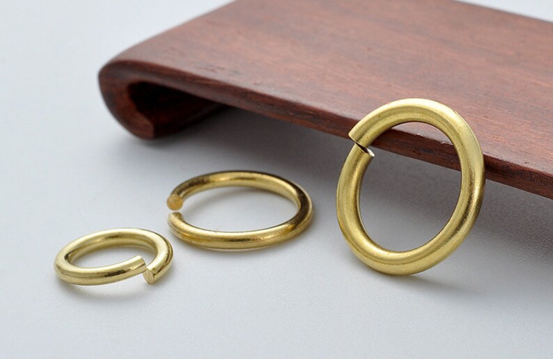 May include: Three gold-colored metal jump rings of different sizes. The rings are open and have a smooth, polished finish.