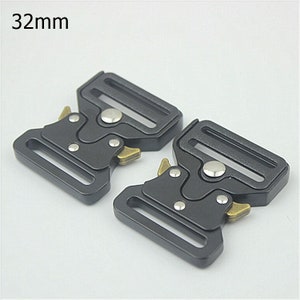 May include: Two black metal belt buckles with a 32mm width. Each buckle has a silver button and gold-colored release levers.