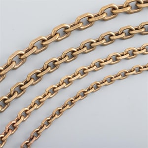 May include: Four gold-colored metal chains of varying sizes are arranged diagonally across a gray background. The chains are made of oval-shaped links, with the largest chain at the top and the smallest at the bottom.