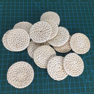 May include: A collection of 10 round, woven, white coasters. The coasters are made from a natural material and have a slightly textured surface.