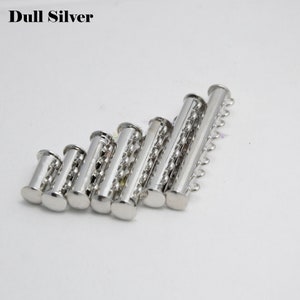 May include: A set of seven silver-toned metal tube clasps for jewelry making. The clasps are arranged in a row from smallest to largest.