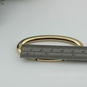 May include: A gold-colored metal oval ring, measuring approximately 3 inches in diameter, is shown on a white surface with a ruler for scale.