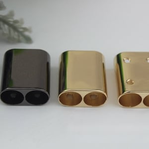 May include: Three metal end caps for a strap or belt. One is black, and two are gold.