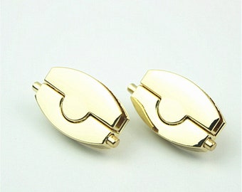 May include: Two gold-colored metal clasps with a unique design. Each clasp has a rounded, oblong shape with a curved cutout and a small cylindrical pin on each end. The clasps are shiny and reflect light.