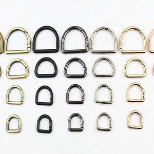 Könnte beinhalten: Sortiment aus Metall-D-Ringen in verschiedenen Größen und Ausführungen, darunter Gold, Silber und Schwarz.