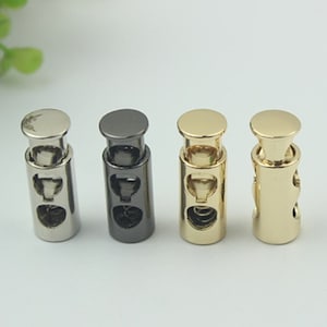 May include: Four metal cord stoppers in different finishes: silver, black, gold, and brass. Each stopper has a spring mechanism to secure cords.