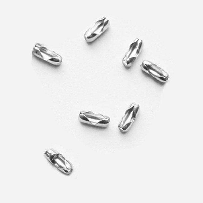 May include: Silver metal chain connectors, scattered on a white surface. These connectors are used to join two chains together.