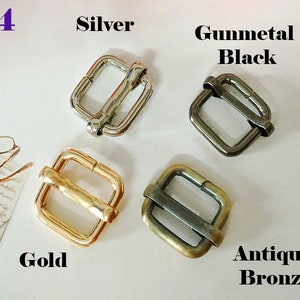 May include: Four metal slider buckles in different finishes: silver, gunmetal black, gold, and antique bronze. Each buckle is square-shaped with a rectangular opening.