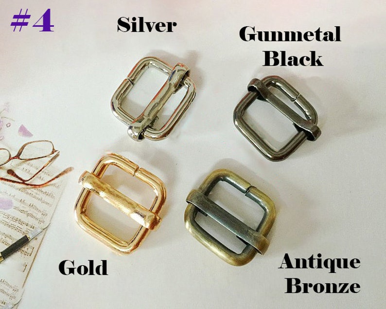 May include: Four metal slider buckles in different finishes: silver, gunmetal black, gold, and antique bronze. Each buckle is square-shaped with a rectangular opening.