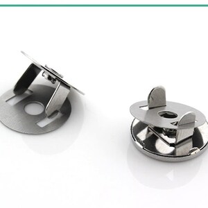 May include: Two silver metal snap fasteners, one with a raised lip and the other with a flat surface.