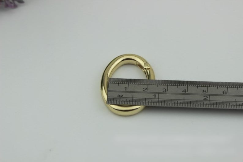 May include: A gold-colored metal oval ring with a swivel clasp, measured against a ruler. The ring is approximately 2 inches in diameter.