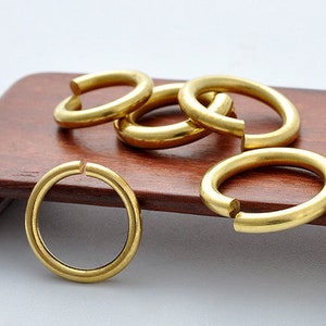 May include: Five gold-colored metal rings, some stacked on top of each other, on a wooden surface.