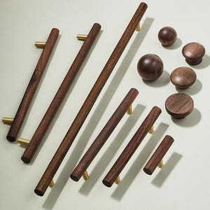 Könnte beinhalten: Ein Satz von acht Holzknauf- und -griffen für Schränke mit Messingakzenten. Die Knöpfe sind rund und die Griffe rechteckig. Die Knöpfe und Griffe sind aus dunklem Holz gefertigt und haben eine natürliche Oberfläche.