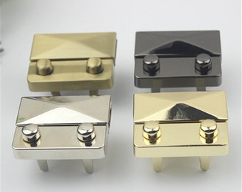 May include: Four metal clasps in different finishes: gold, silver, brass, and black. Each clasp has a square shape with a raised, diamond-shaped design and two round studs.