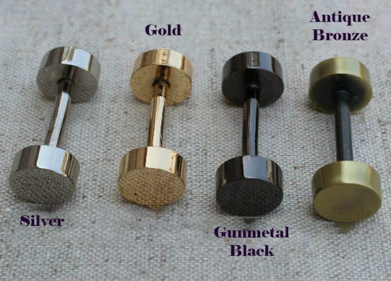 May include: Four dumbbell-shaped stud earrings in silver, gold, gunmetal black, and antique bronze. Each earring has a cylindrical post connecting two flat, round discs. The text labels each color: Silver, Gold, Gunmetal Black, and Antique Bronze.