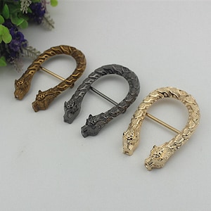 May include: Three metal belt buckles in gold, silver and black, each featuring a dragon head design.